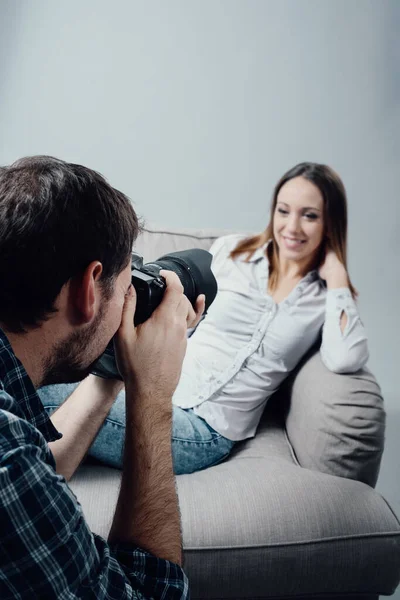 摄影棚里的专业摄影 一个女模特坐在扶手椅上笑着 摄影师用他的数码相机拍照 — 图库照片