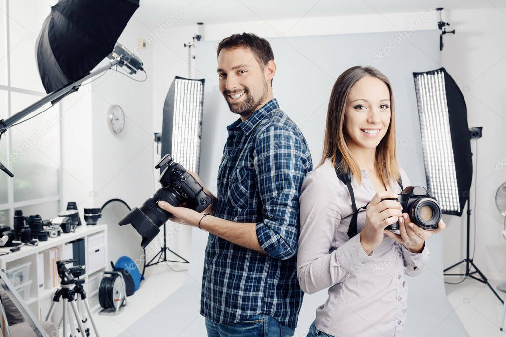 Smiling young professional photographers posing in the studio, they are holding digital cameras