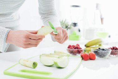 Mutfakta meyve hazırlayan kadın, kesme tahtasındaki elmaları kesip soyuyor.