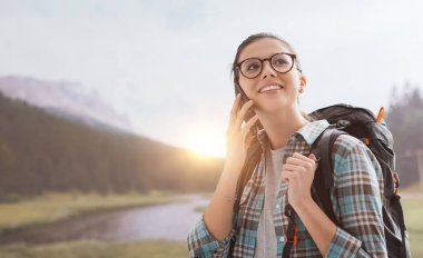 Dağlarda yürüyen ve cep telefonuyla telefonla konuşan gülümseyen bir kız.