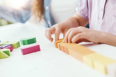 Renkli oyuncak tahta bloklarıyla oynayan bir kız, annesi ona yardım ediyor, eğitim ve eğlence kavramı.