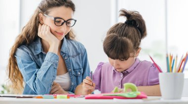 Genç gülümseyen öğretmen ve yaratıcı tatlı kız okulda birlikte resim çiziyorlar.