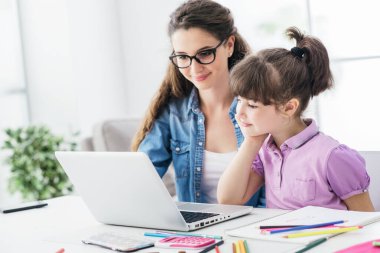 Genç öğretmen ve tatlı kız birlikte dizüstü bilgisayar kullanıyor ve online, teknoloji ve eğlence konseptini birbirine bağlıyor.