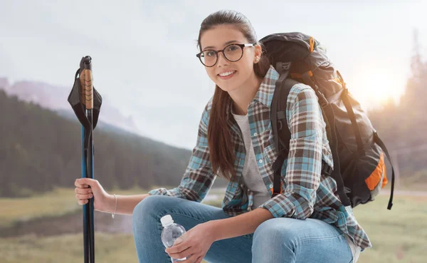 面带微笑的女人在山上跋涉 休息一下 然后坐着 拿着远足的手杖 — 图库照片