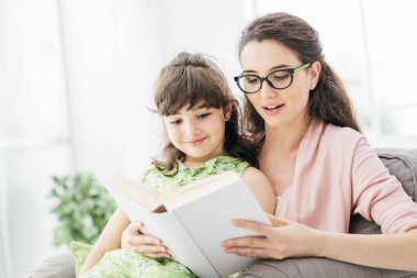Anne ve kızını seven ve evinde birlikte dinlenen kadın, kıza bir masal okuyor.