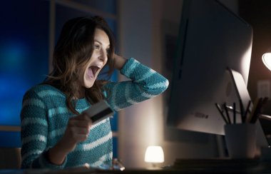 Kredi kartı tutan ve bilgisayarında online alışveriş yapan neşeli mutlu bir kadın, teklifler ve şok edici indirimler buluyor.