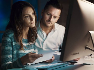 Bir çift sözleşmeyi okuyor, detayları kontrol ediyor ve bilgisayarlarıyla bağlantı kuruyor. Endişeli ve hayal kırıklığına uğramış durumdalar.