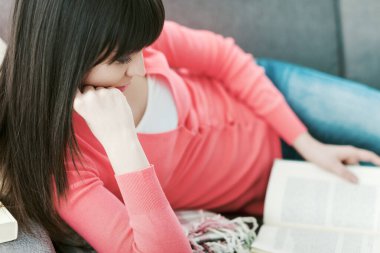 Çekici bir kadın evdeki kanepede uzanıp ilginç bir kitap okuyor, rahatlıyor ve rahatlıyor.