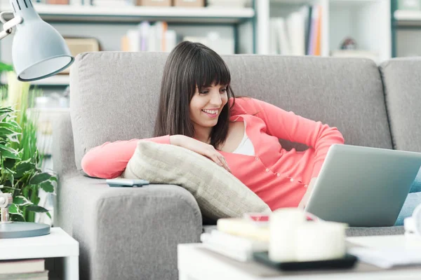 年轻的微笑的女人在家里 她正在沙发上放松 还在用笔记本电脑社交 — 图库照片