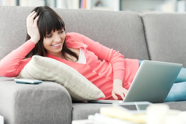 年轻的微笑的女人在家里 她正在沙发上放松 还在用笔记本电脑社交 — 图库照片