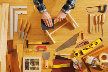 Erkek eller işe yarar bir taburede çalışıyor yüzeyi düzleştiriyor, her yerde DIY araçları, üst görünüm