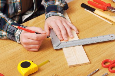 Bir DIY projesinde çalışan ve her yerde iş aletleri olan ahşap bir kalas ölçen bir adam, eller kapalı.