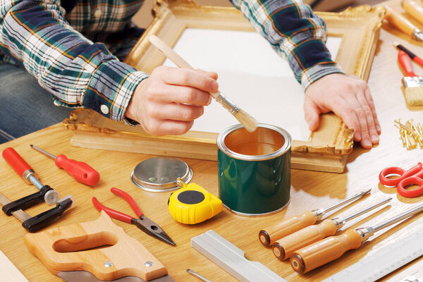 Decorator varnishing a wooden frame hands close up with DIY tools, hobby and craft concept