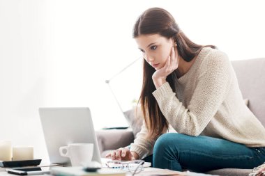 Evdeki kanepede dinlenen ve dizüstü bilgisayar, teknoloji ve iletişim konsepti kullanan bir kız.