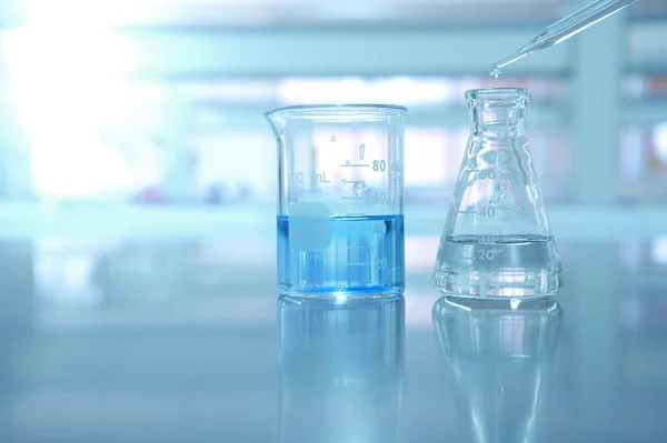 Főzőpohár, és a lombikot kék megoldás, és a csepp víz a tudomány — Stock Fotó