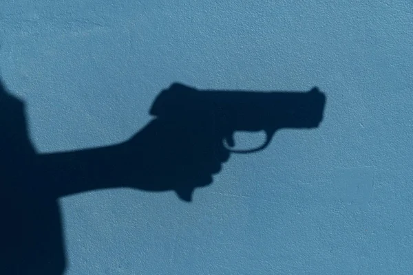 shadow of hand holding gun on blue cement wall background in vio