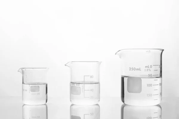 Trois taille de bécher en verre avec de l'eau sur le laboratoire médical blanc — Photo