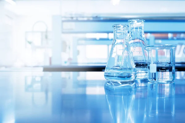 Acqua in becher e fiaschetta di vetro in chimica blu scienza labora — Foto Stock