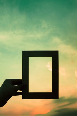 Siyah siluet kadın elinde dramatik mavi günbatımı gökyüzü arka planında resim çerçevesi tutuyor.