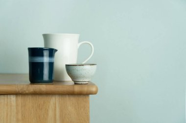 Beyaz seramik bardak ve çay fincanı doğanın ahşap masasının üzerinde. Yiyecek içeceği ve arka plan için klasik mavi beton duvarlı.