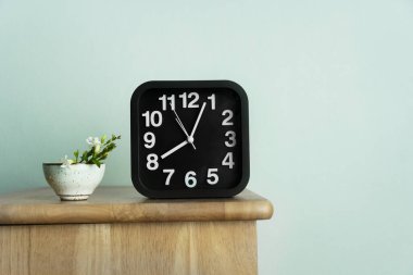 Çay fincanı seramiği, yabani yeşil çiçek ve siyah saat. Sabahları ahşap masa ve mavi arka plan üzerinde.