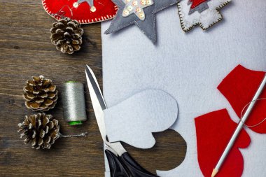 Parlak Noel oyuncaklar keçe ile yapılmış. Makas, kalem, iplik ve diken üstünde ahşap bir masa.