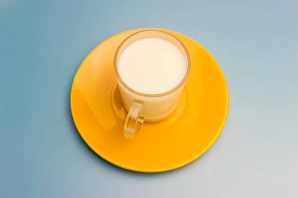 Latte in una tazza di vetro su un piattino giallo — Foto Stock