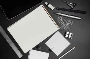 Ofis malzemeleri siyah arka planda. Not defteri, cetvel, kalem, kalem, ataç, bileyici. Çalışma alanı, üst manzara. Metnin altına yerleştir.