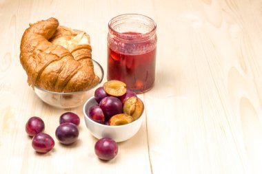 Cam kavanozda ev yapımı erik reçeli. Erik reçeli, kruvasan ve olgun erikler arka planda. Yüksek anahtar. Seçici odak