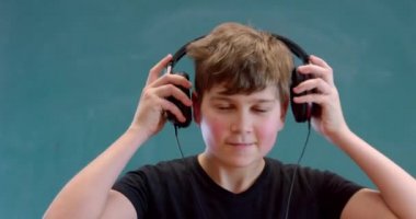 Siyah kulaklıkla müzik dinleyen ve yeşil arka planda dans eden mutlu küçük çocuk.