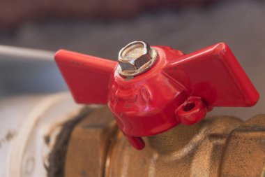 A shut-off valve painted in shiny red paint is located on the central heating pipe. Damage is visible on the surface of the paint. Traces of metal processing are on a metal nut. Soft focus. clipart