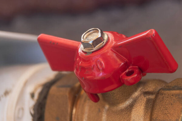 A shut-off valve painted in shiny red paint is located on the central heating pipe. Damage is visible on the surface of the paint. Traces of metal processing are on a metal nut. Soft focus.
