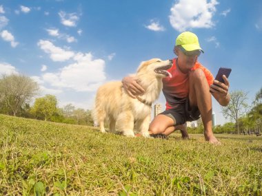 Evde beslenen hayvan köpek sahibi bir şehir parkı ile kameraya bakıyor. Beyaz sarı renk ve fazla saç köpek yavrusu.