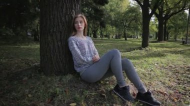 Yalnız kız spor formunda bir ağacın altında oturup bıkkın