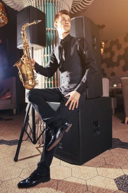 Oturma ve saksafon tutan genç adam