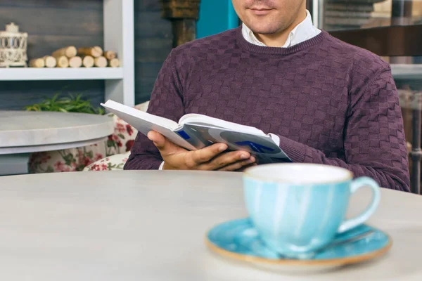 Młody człowiek siedzi w kawiarni i czyta książkę — Zdjęcie stockowe