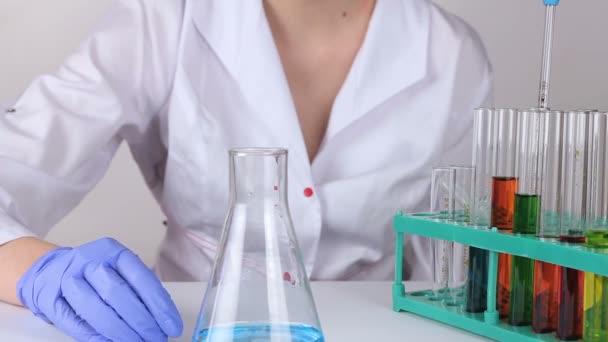 A young woman doctor stirs the liquid in a flask. — Stock Video