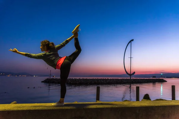 Bir kadın, gün batımında İsviçre 'de Lozan' da yoga egzersizleri yapan bir heykelle gölün önünde duruyor.