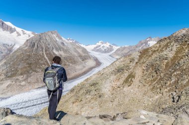 Sırtında sırt çantasıyla genç beyaz bir kadın Aletsch Buzulu 'na bakıyor. 23 km boyunca uzanan dev bir buz akıntısı.