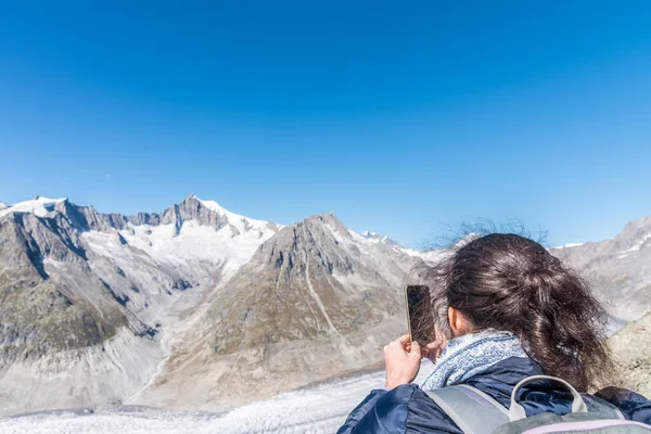 Aletsch Buzulu 'nu Eggishorn' dan, Bernese Alpleri 'nden, Valais Kantonu' ndan, İsviçre 'den, Avrupa' dan akıllı telefonla çeken kadının arka görüntüsü.