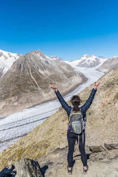Kollarını kaldırıp Eggishorn, Bernese Alpleri, Valais kantonu, İsviçre, Avrupa 'dan Aletsch Buzulu' na bakan bir kadının arkasından bakın.