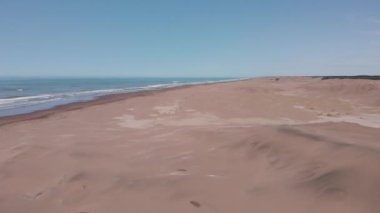 Kum tepelerinin üzerinde ve ufukta deniz kıyısının panoramik görüntüsü var. Bulutlu gökyüzü.