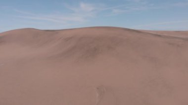 Kum tepeciklerinin arkasında daha fazla kum tepesi ve bitki örtüsü var..