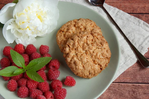 Delicious cookies with raspberries, mint and white peony flower on the plate.