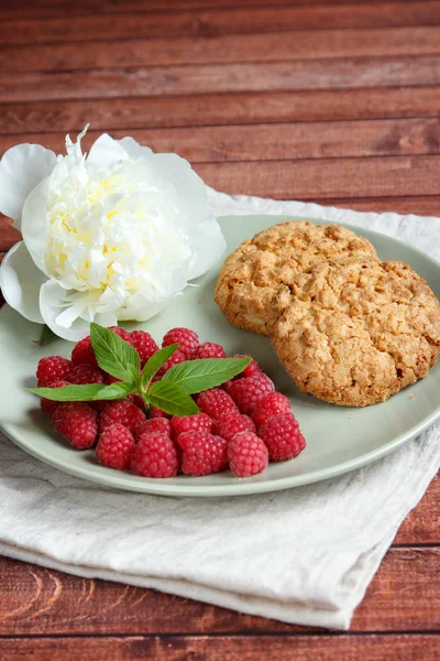 Delicious cookies with raspberries, mint and white peony flower on the plate.