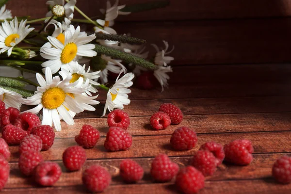 Eine Handvoll reife Himbeeren und Kamillenblüten auf einem Holzbrett — Stockfoto