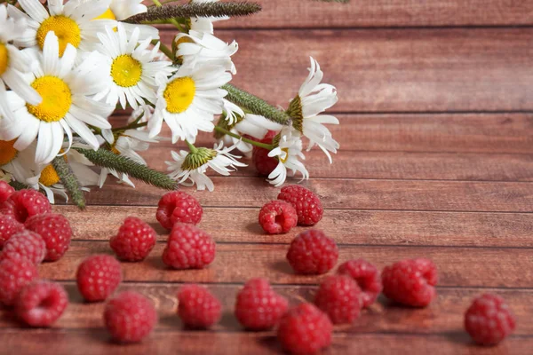 Eine Handvoll reife Himbeeren und Kamillenblüten auf einem Holzbrett — Stockfoto