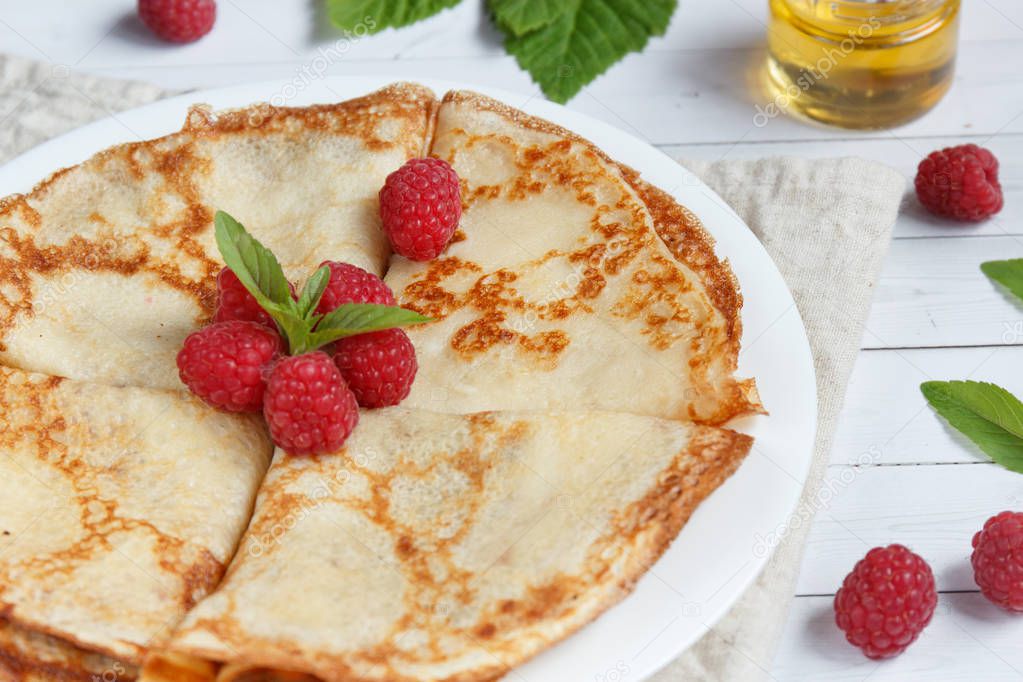 Thin pancakes with honey and raspberries on a white plate