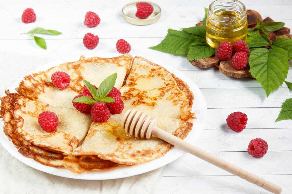 Thin pancakes with honey and raspberries on a white plate