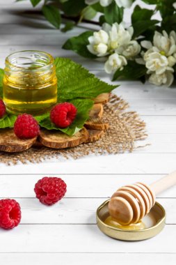 Tatlım, çilek ve ahududu yaprağı bir ahşap stand bir kase. Kaşık bal, Yasemin çiçekleri ile